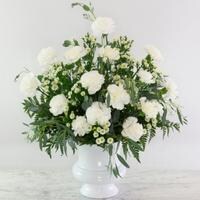 A white sympathy urn filled with white carnations, white roses, and foliage.